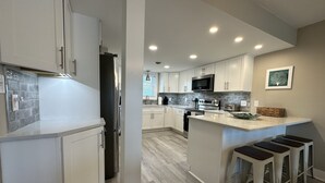 Una cocina moderna con armarios blancos, una isla central con taburetes, un microondas y un refrigerador de acero inoxidable.