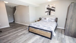 A bedroom with a bed, a nightstand, a wall-mounted abstract painting, and a wardrobe.