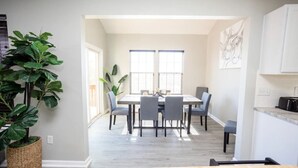 A dining area with a table and chairs, a large potted plant, and a view of the kitchen.