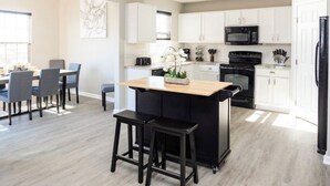A modern kitchen with white cabinets, a central island with stools, and a dining area with a table and chairs.