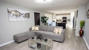 A modern living room with a grey sectional sofa, a glass coffee table, and a painting on the wall.