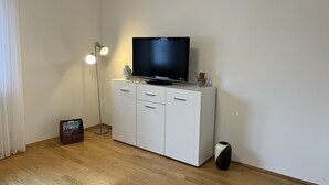 A room with a white cabinet, a flat-screen TV on top, a floor lamp, and a small table with a vase and a glass. - Oberursel old town very centrally located (Oberursel)