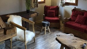 A cozy living room with a wooden chair, a red sofa, a small stool, and a wooden table.