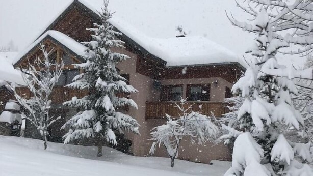 A snow-covered building with a sloped roof, surrounded by snow-laden trees.