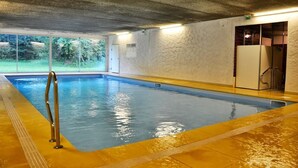 Una piscina interior amb aigua cristal·lina, un espai de socors i una porta que dona a un vestidor.