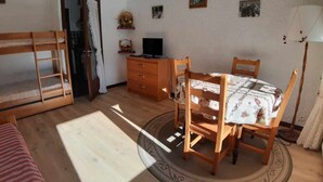 Una habitació amb literes, un escriptori de fusta, una taula de dinar amb cadires i una làmpada.