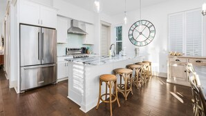 Een moderne keuken met witte kastjes, een roestvrijstalen koelkast, een groot eiland met barkrukken, en een ronde wandklok.