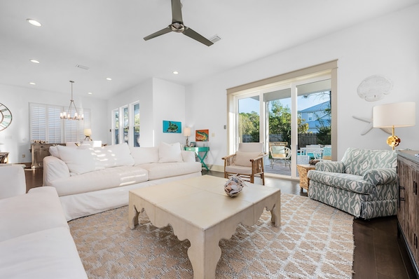 A spacious living room with a white sofa, a coffee table, and a patterned rug. There is a large window with a view of the outdoors.