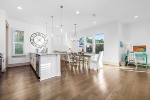 A spacious kitchen with a central island, pendant lighting, and a large wall clock.