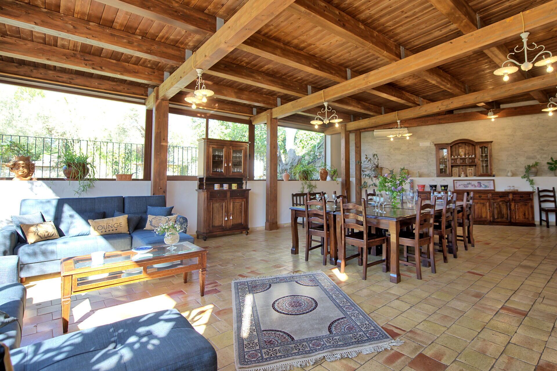 A spacious living area with a wooden ceiling, a dining table set for six, and a sofa with a patterned rug.