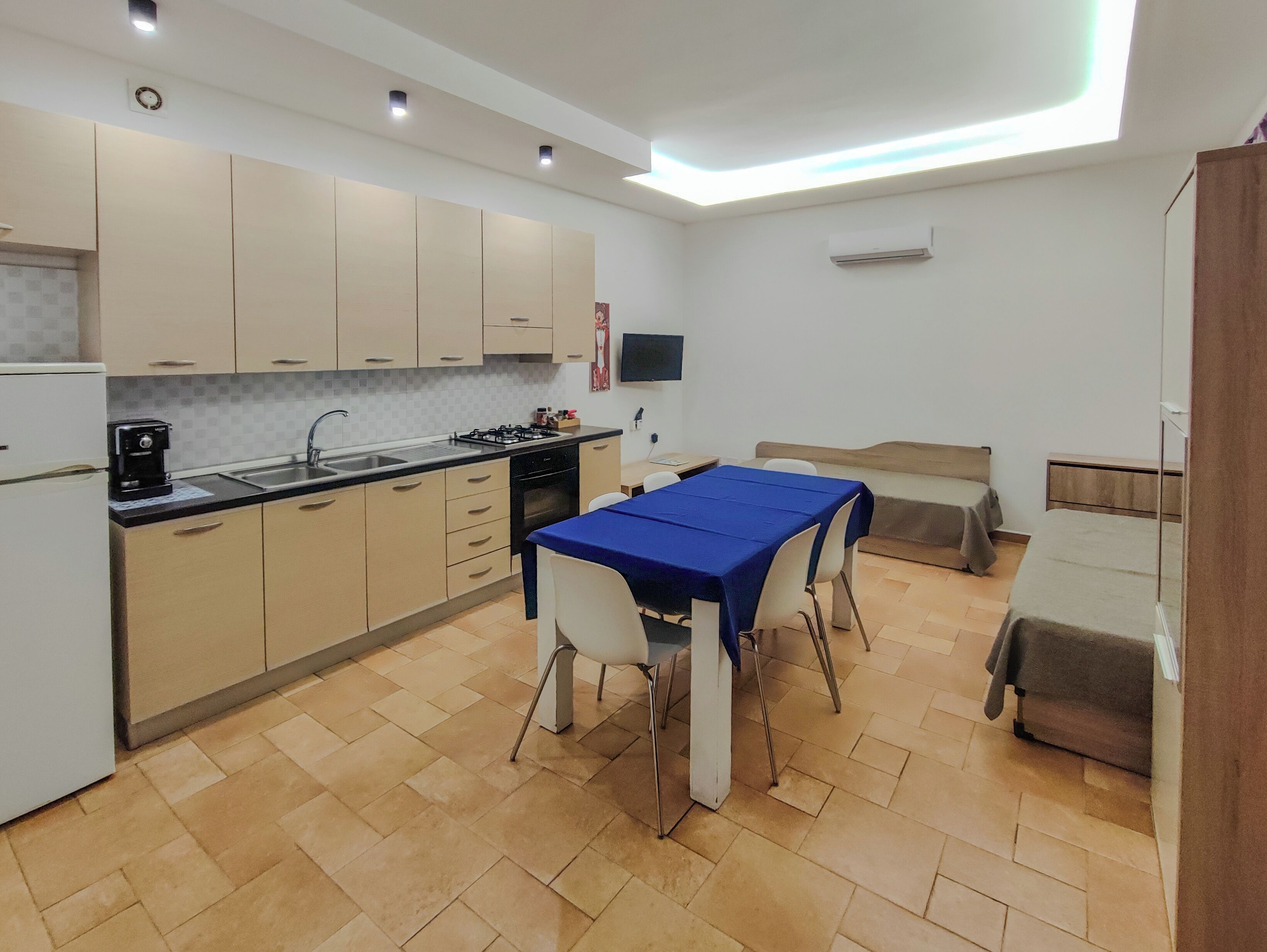 A modern kitchen with a dining area, a flat-screen TV mounted on the wall, and a built-in air conditioning unit.