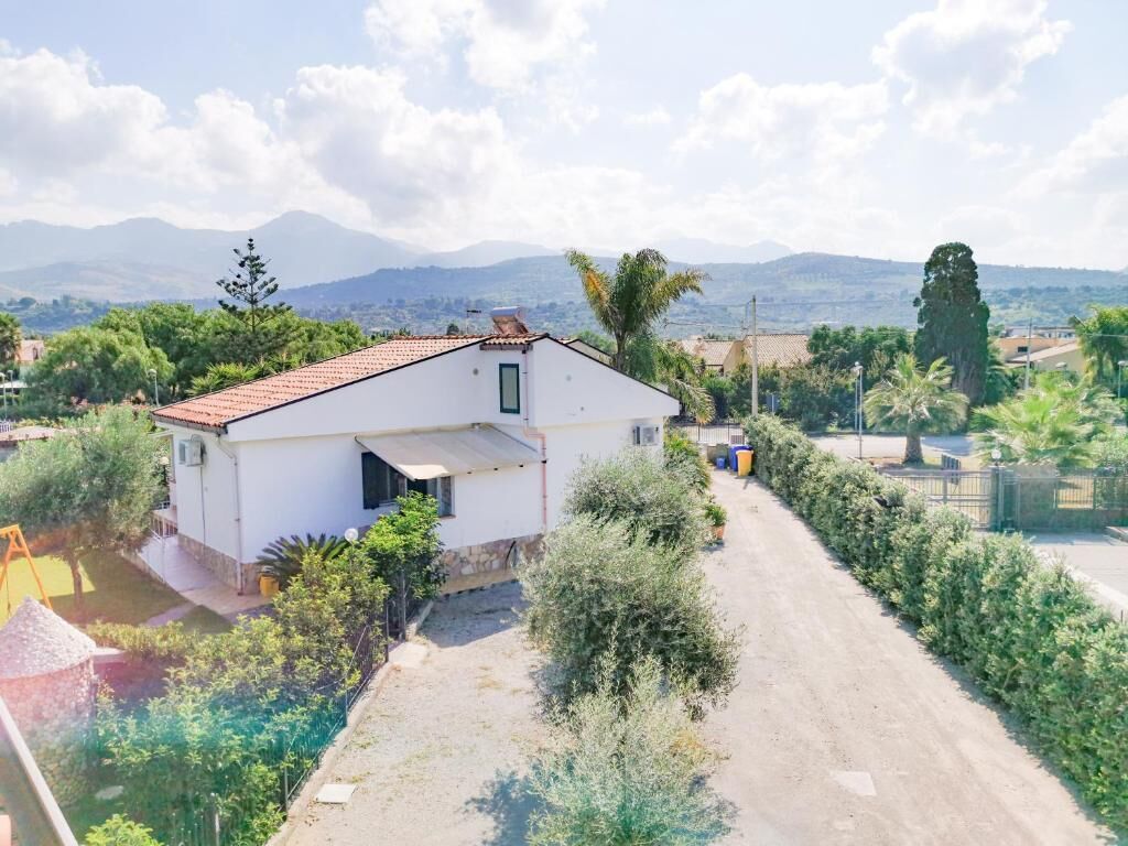 Una casa blanca con techo rojo, rodeada de follaje y un sendero de tierra.