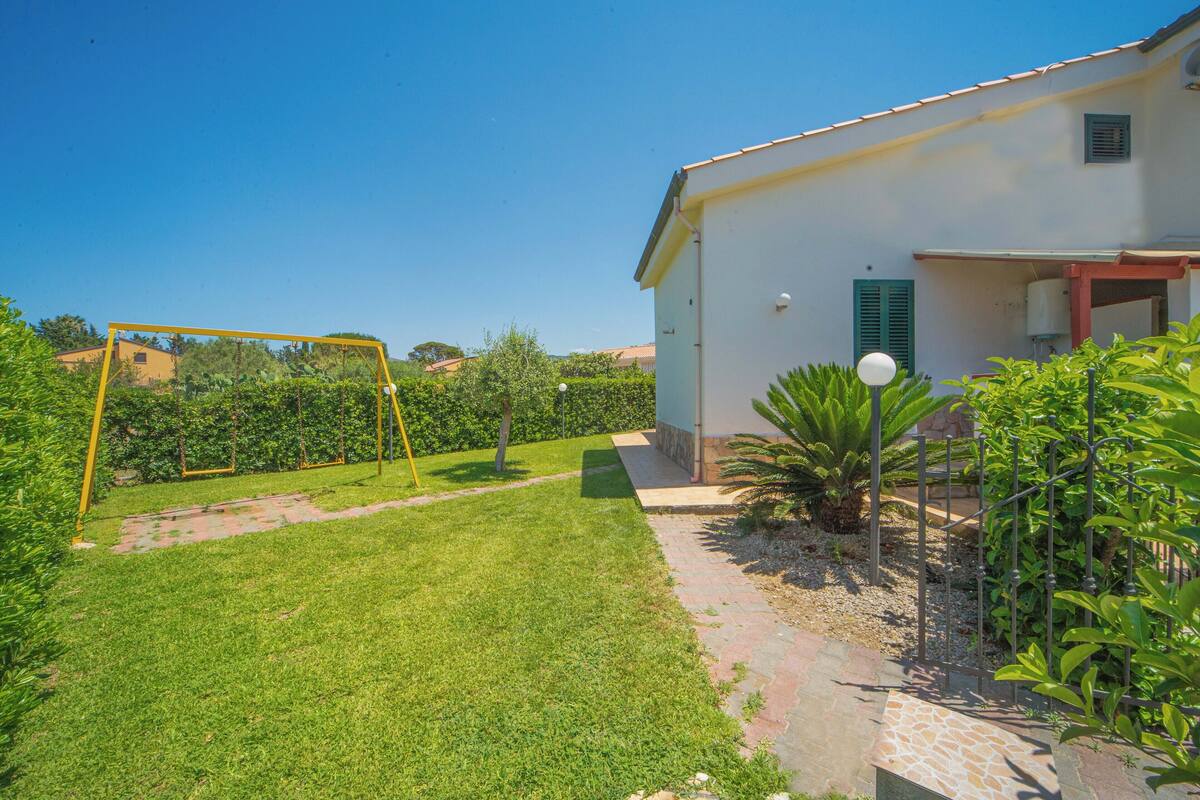 A house with a well-maintained lawn, a swing set, and a small garden area with various plants.