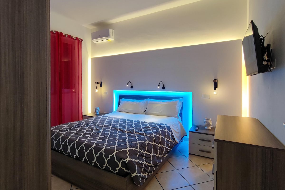 A modern bedroom with a bed, bedside tables, a nightstand, and a wall-mounted TV.