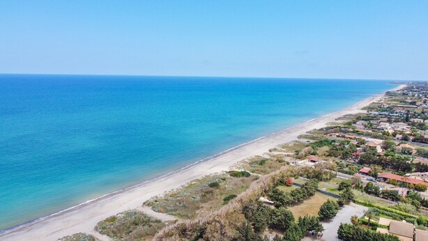 Luchtbeeld van een kustgebied met strand, woongebouwen en begroeiing.