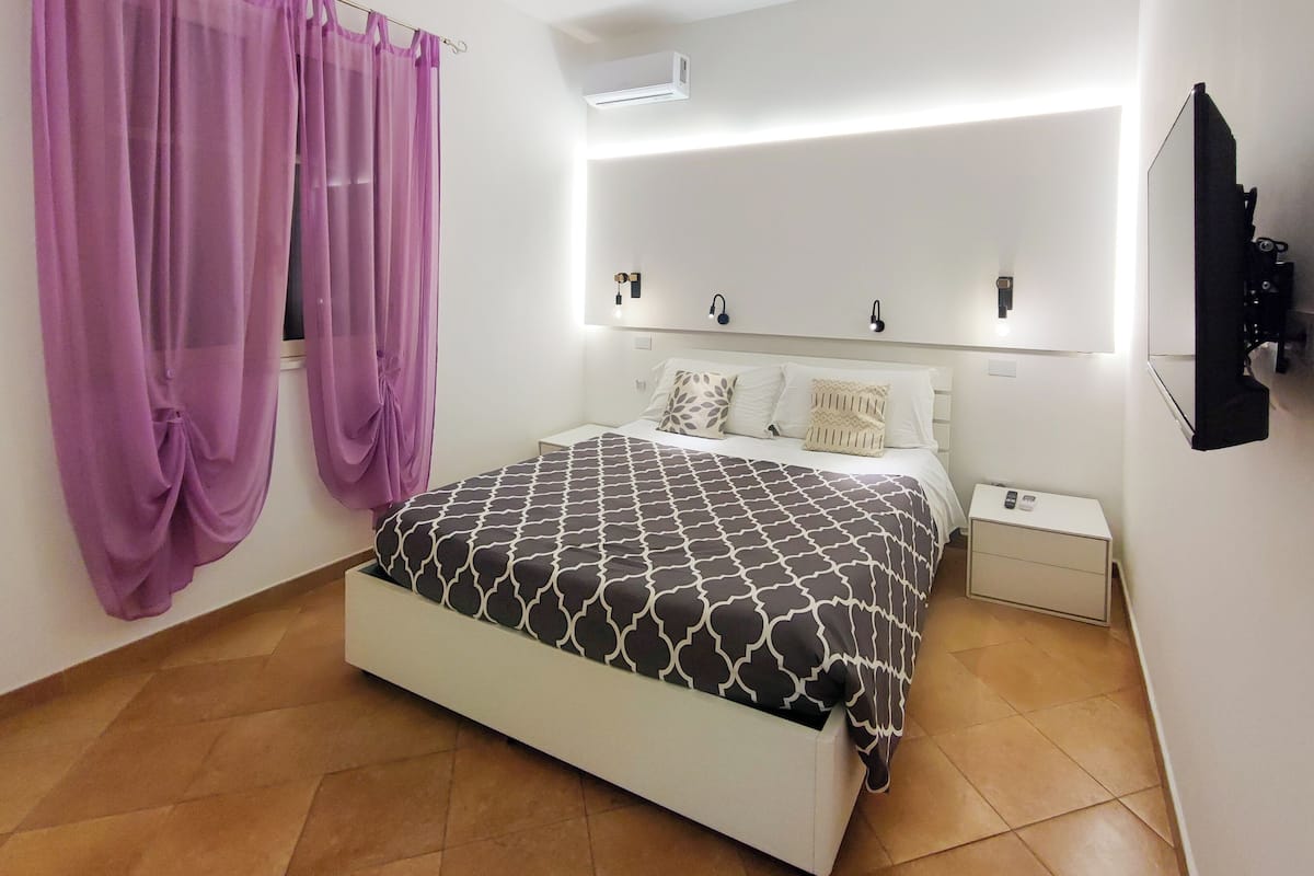 A bedroom with a bed, curtains, bedside tables, and a wall-mounted TV.
