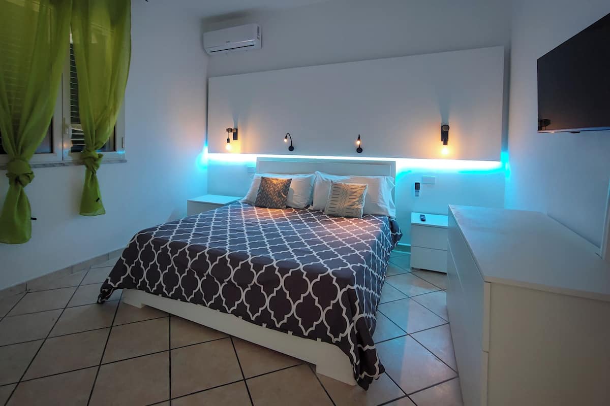 A modern bedroom with a patterned bedspread, bedside lamps, and a wall-mounted air conditioner.