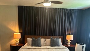 Ett hotellrum med en stor säng, två sänglampor, en takfläkt och en värmare.