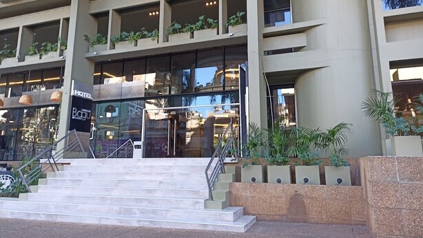 Hotel amb disseny arquitectònic modern, amb una entrada destacada amb portes de vidre, una escala que condueix a l'entrada i múltiples balcons amb vegetació.