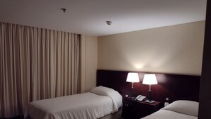 Habitació d'hotel amb dos llits, una tauleta de nit amb una làmpada i una cortina.