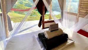 Una habitación con cama, un cartel de bienvenida y vistas a un paisaje verde a través de cortinas translúcidas.
