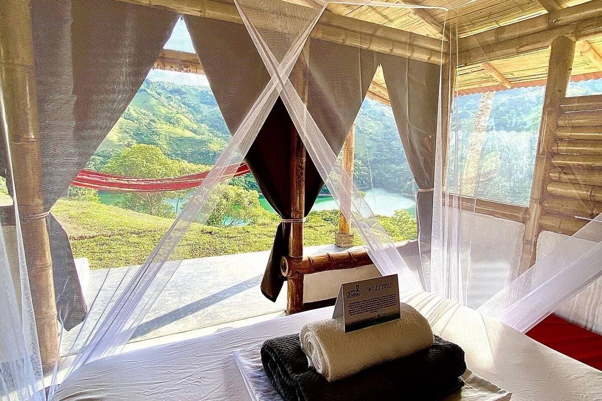 Una habitación con cama, un cartel de bienvenida y vistas a un paisaje verde a través de cortinas translúcidas.
