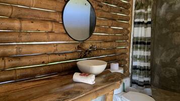 Une salle de bain avec un mur en bois, un miroir rond, un lavabo blanc, des toilettes et un rideau de douche.