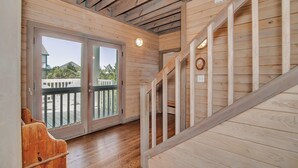 Et træinteriør med trappe, en glasdør der fører ud, samt udsigt til et hvidt hegn og grøn bevoksning.
