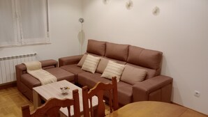 A living room with a brown sofa, a wooden dining table, and a window with white curtains. - Nice apartment in Candás (Candás)