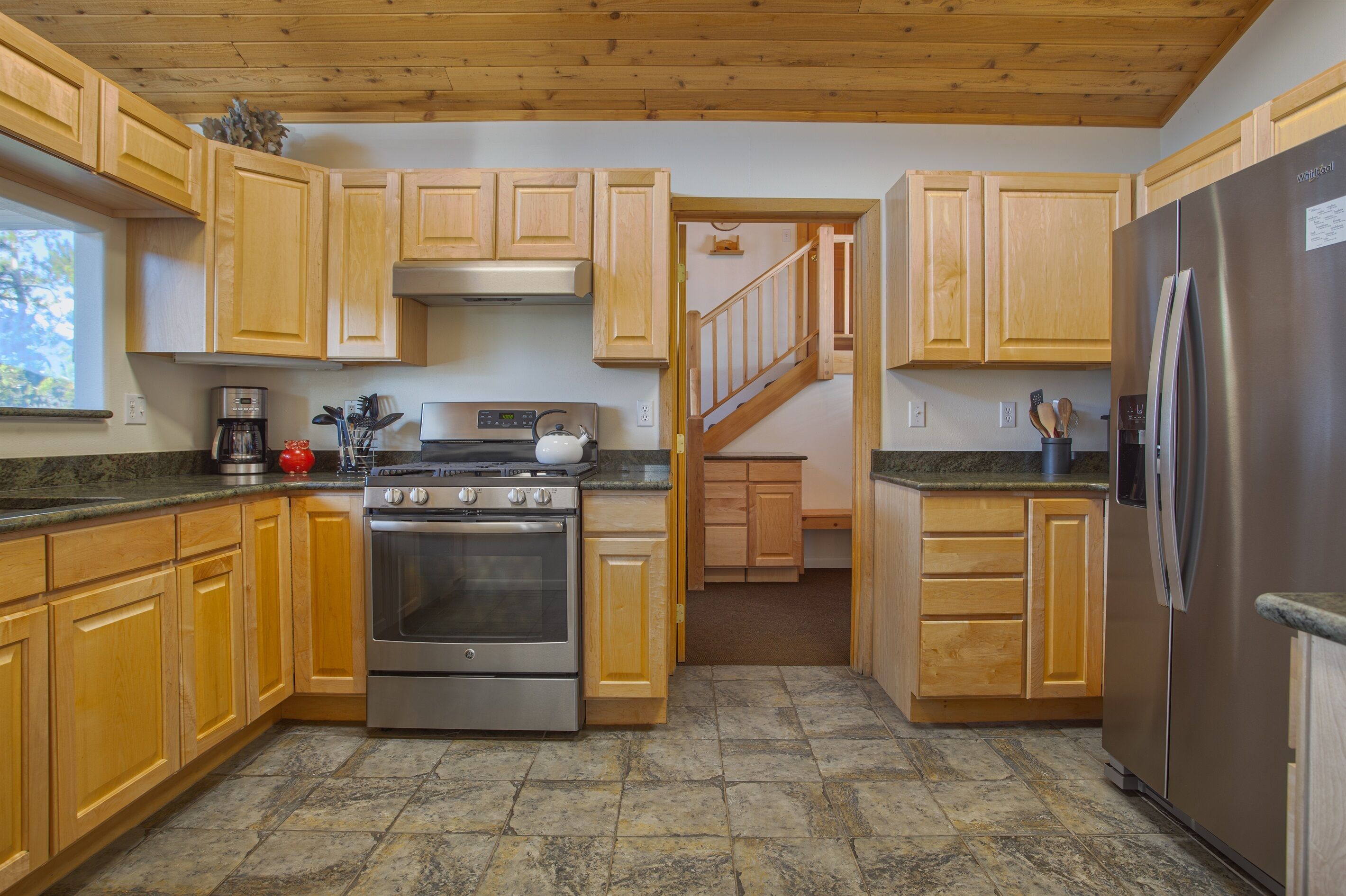 A kitchen with wooden cabinets, a stainless steel refrigerator, a stove, and a coffee maker.