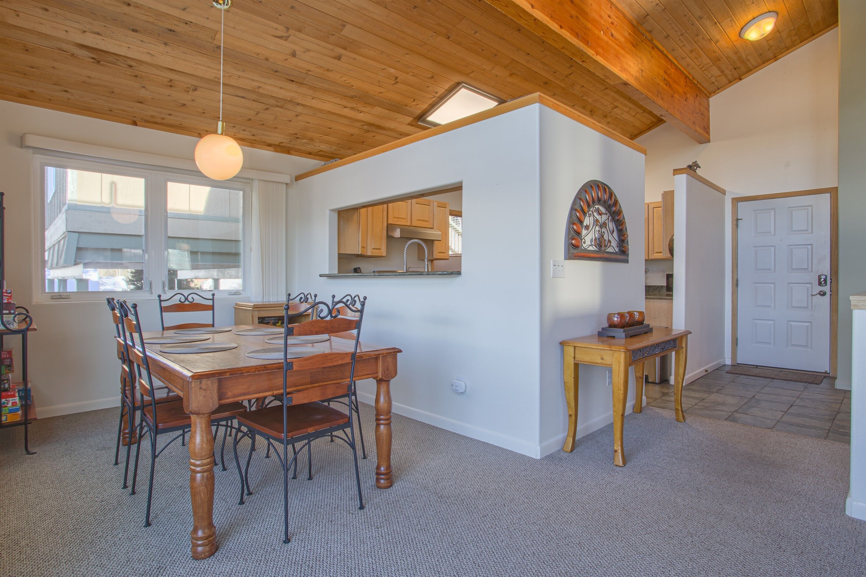 A dining area with a wooden table and chairs, a small kitchen with a window, and a door leading to another room.