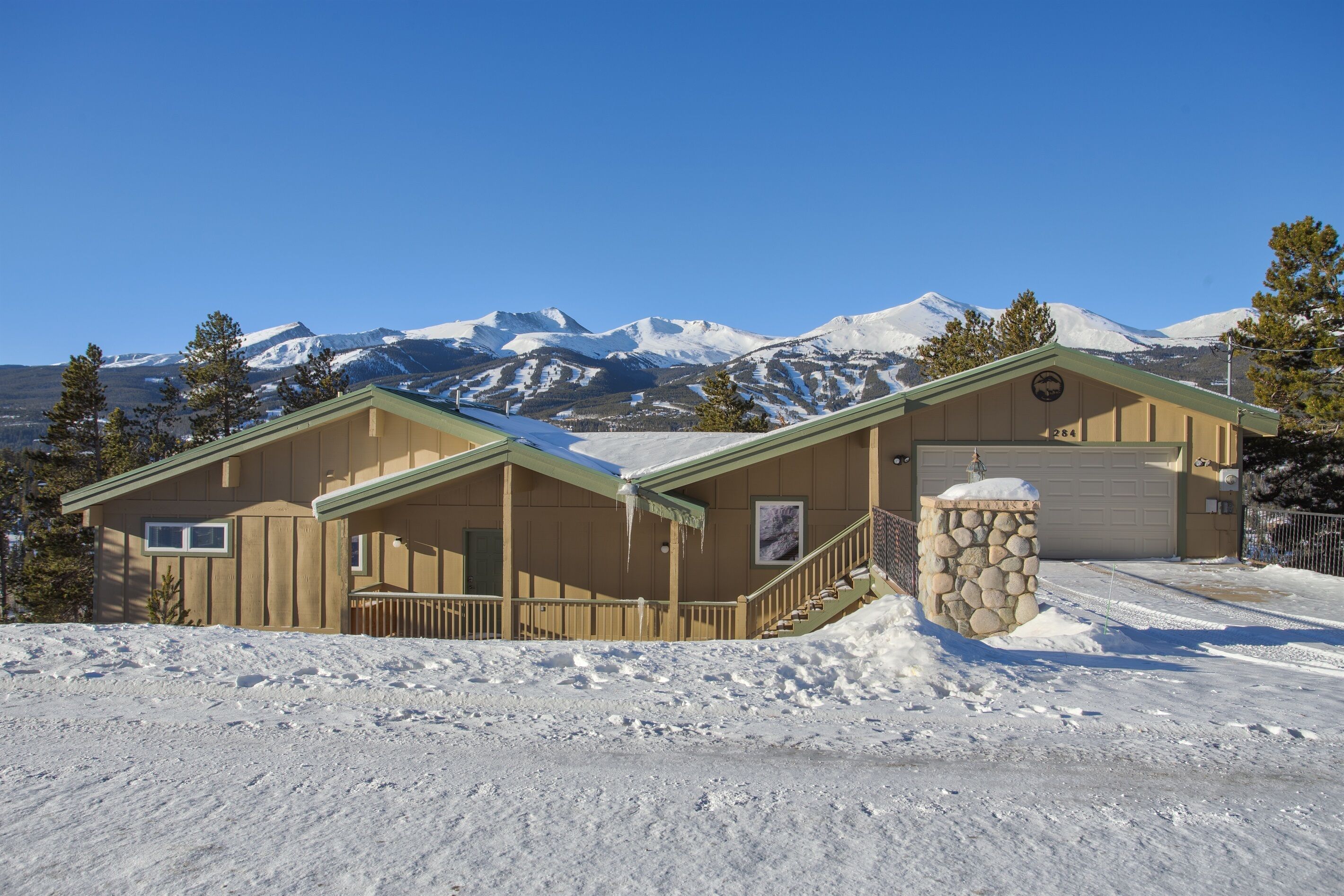 A lodge with a stone entrance, a covered porch, and a view of snow-capped mountains.