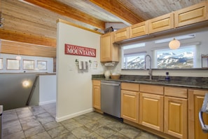 A kitchen with wooden cabinets, a stainless steel dishwasher, and a window with a mountain view.