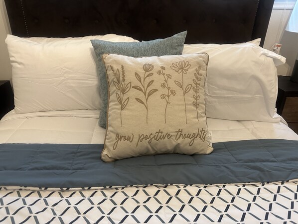 A bed with a patterned bedspread, a decorative pillow with floral embroidery, and a dark headboard.