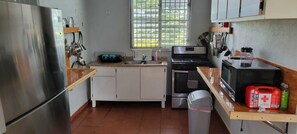 A compact kitchen with a stainless steel refrigerator, a microwave, and a stove. There is a window with blinds, a sink, and cabinets.