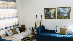 A living room with a blue sofa, a blue armchair, a small wooden table with a plant, and a teddy bear. - 250picnics (Kigali)