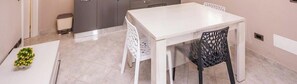 A white dining table with a black chair, a small trash bin, and a potted plant.