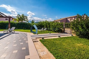 A courtyard with a tiled patio, lounge chairs, and a well-maintained lawn. - Ricky villa by the sea, pure relaxation (Sicilia)