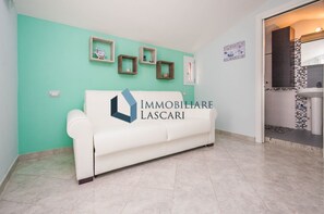 A white sofa against a teal wall with three framed items above it.