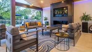 A modern living room with a fireplace, sofas, and a large TV screen displaying 'Overnight DIGG Luxury Vacation Rentals.' - Lakefront Home with Pool, Game Room & Dock (Hot Springs)