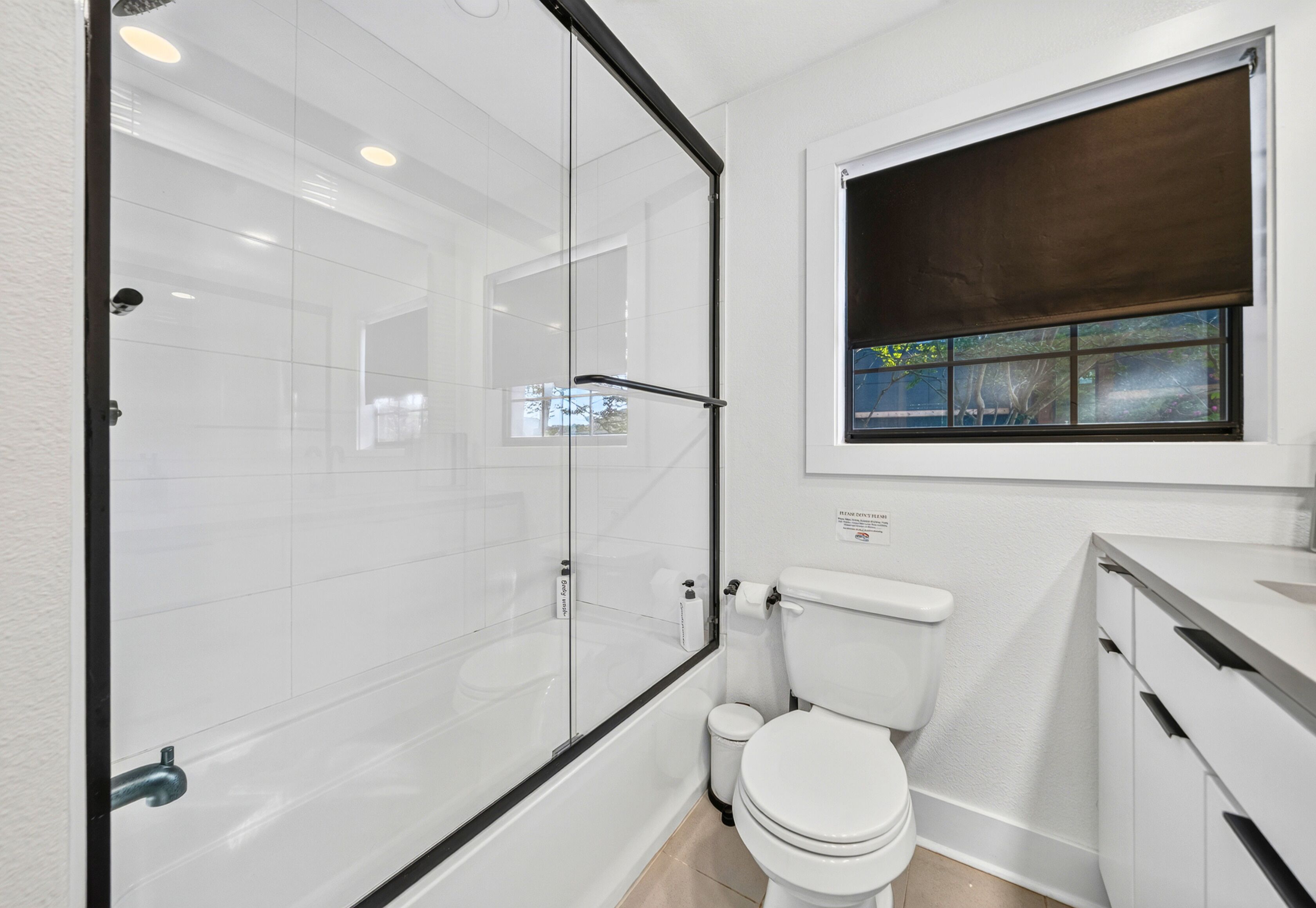 A bathroom with a glass shower enclosure, a toilet, and a window with a view of trees.