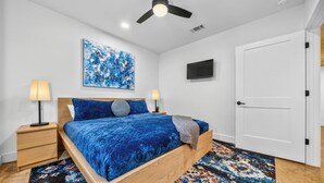 A bedroom with a bed, two bedside tables, a ceiling fan, a TV, and a door. - Lakefront Retreat w/Hot Tub, Fire Pit, Games! (Hot Springs)