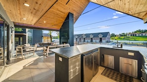 Un área de cocina al aire libre con techo de madera, electrodomésticos integrados y vistas a un barrio residencial.