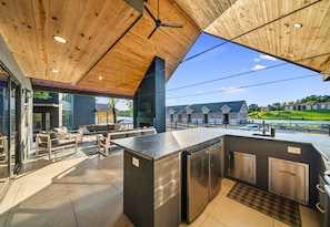 An outdoor kitchen area with a wooden ceiling, built-in appliances, and a view of a residential neighborhood.