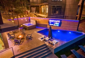 Zona de piscina en la azotea con hidromasaje, sillas de descanso y una pantalla de televisión.