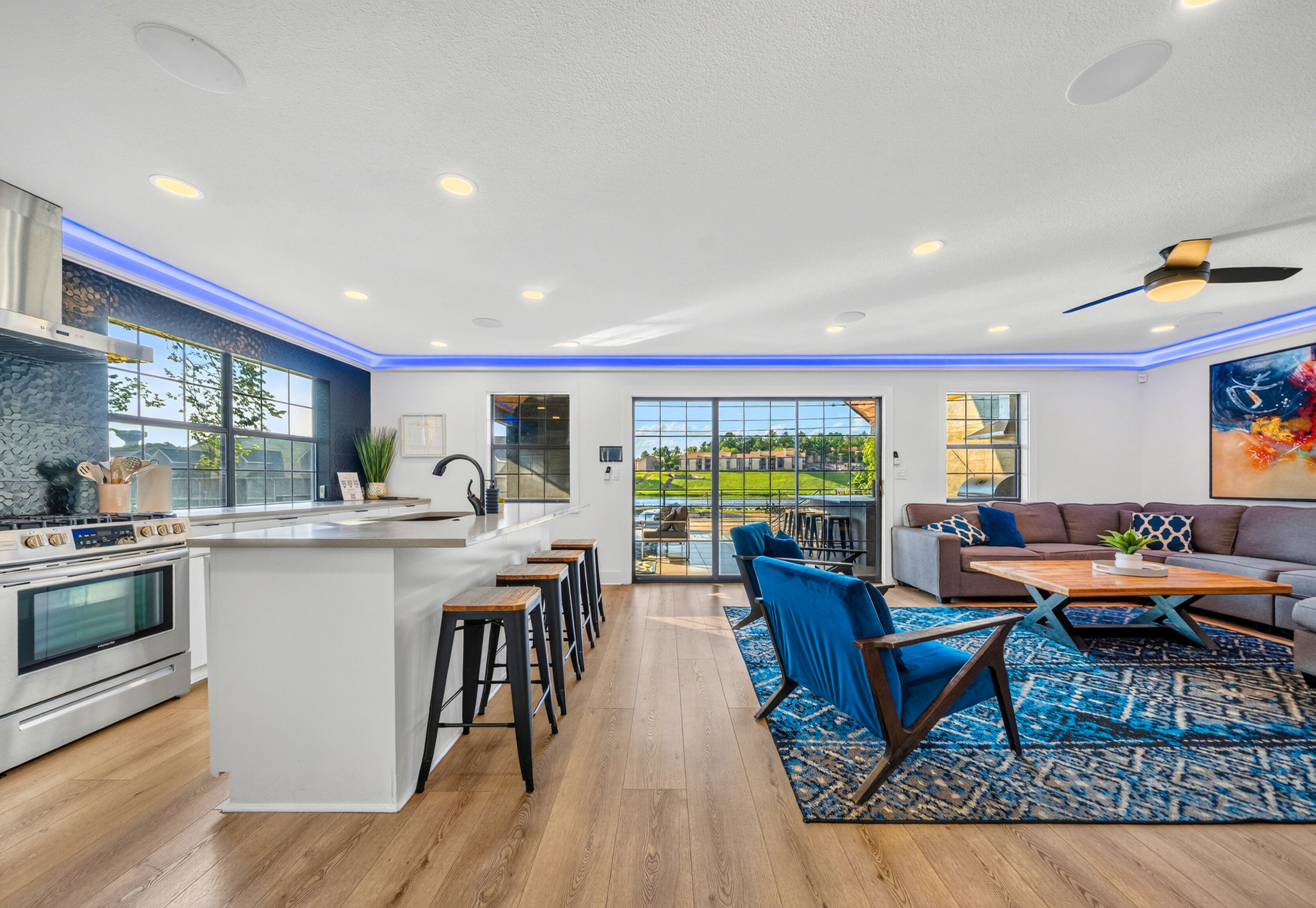 A modern kitchen with a central island, bar stools, and a dining area with a blue patterned rug.