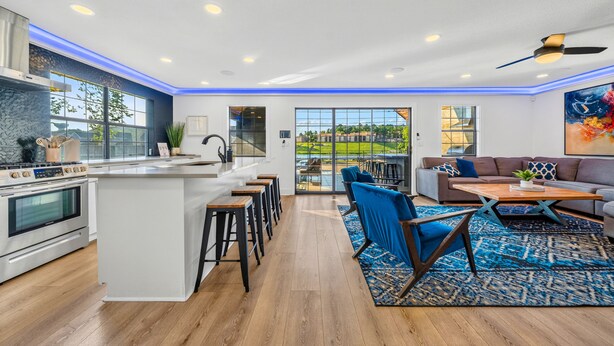 A modern kitchen with a central island, bar stools, and a dining area with a blue patterned rug. - Lakefront Retreat w/Hot Tub, Fire Pit, Games! (Hot Springs)
