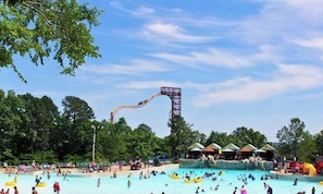 A water park with a large pool, a water slide, and several shaded areas.