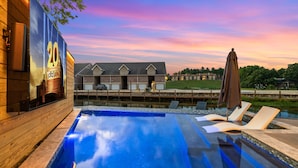 A swimming pool with lounge chairs, a wooden deck, and a building with a 20th anniversary sign in the background. - Lakefront Retreat w/Hot Tub, Fire Pit, Games! (Hot Springs)