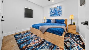 Un dormitorio con cama, ventilador de techo, un cuadro y una alfombra estampada.